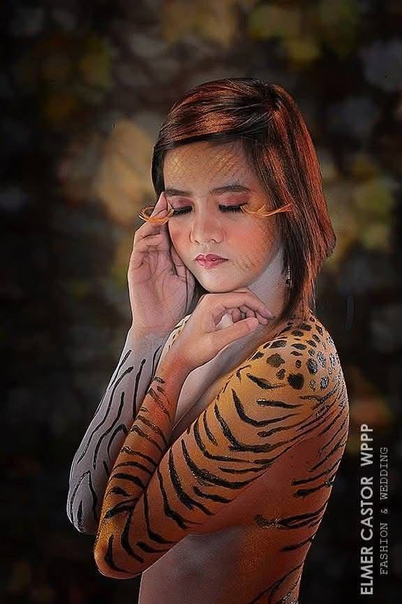 Model with tiger-stripe body paint in orange and black across her shoulder and arm, veiled in sheer netting.