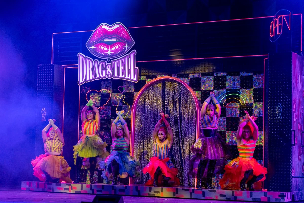 Drag performers in colorful costumes and bold stage makeup performing under neon lighting.